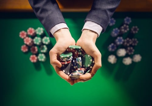 homme élégant tenant dans sa main des jetons de casino au-dessus d'une table sur laquelle sont disposés d'autres jetons