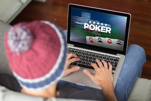 jeune homme jouant au poker en ligne depuis son ordinateur sur son sofa